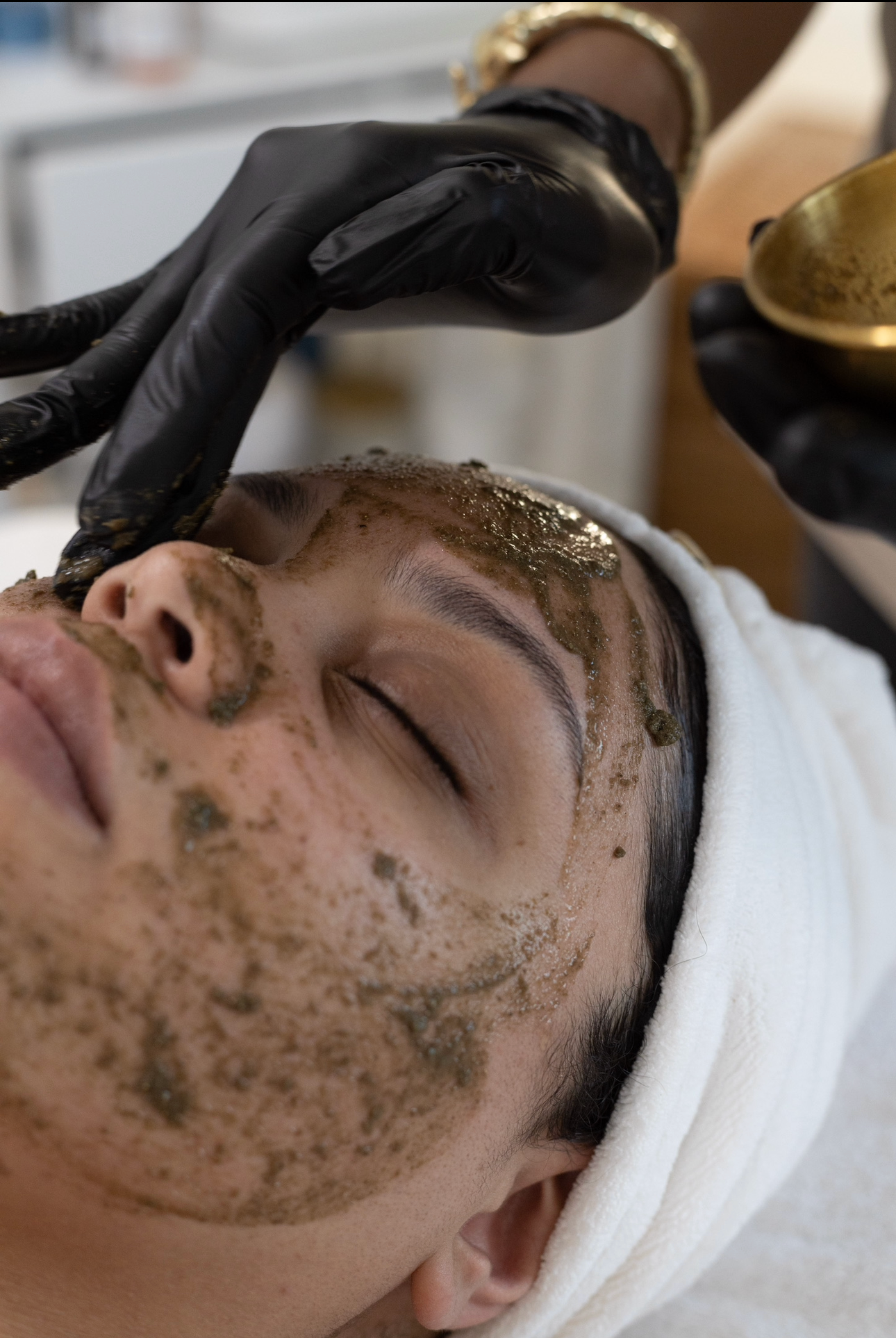 Person receiving a facial treatment with black gloves applying a product to their face.